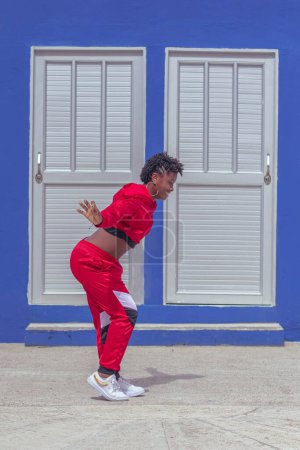 Photo for Jover mujer afro realiza baile estilo urban en parque local con pared azul y puertas de fondo - Royalty Free Image
