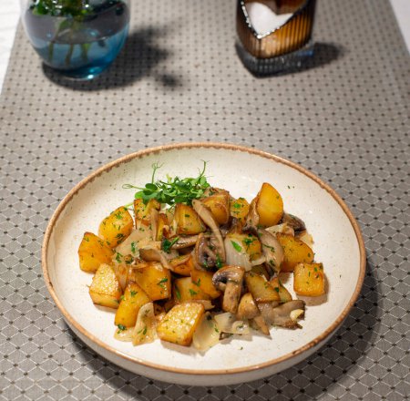 Bratkartoffeln mit Rosmarin auf weißem Teller auf einem Holztisch mit Serviette