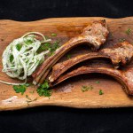 grilled lamb ribs with herbs and spices on black slate board.