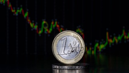 Téléchargez les photos : A coin in denomination of 1 euro stands on a computer keyboard against the background of a stock summary chart - en image libre de droit