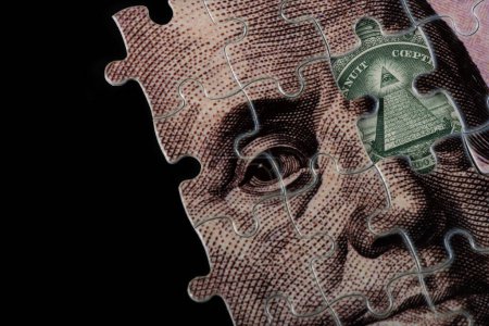 Jigsaw puzzle with a portrait of Benjamin Franklin from a 100 US dollar bill and a fragment of a 1 US dollar bill with a pyramid and an all-seeing eye