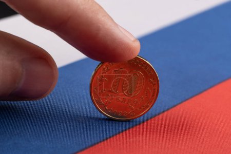 A man's finger keeps a coin of 10 Russian rubles from falling on the flag of the Russian Federation