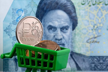 Photo for A coin with the symbol of the Russian rudl in a miniature shopping cart against the background of an Iranian banknote - Royalty Free Image