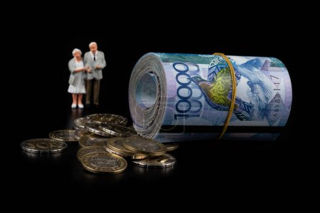 Foto de Billetes laminados de 10.000 tenge kazajos, monedas de 100 y 200 tenge denominaciones y figuritas de una pareja de ancianos sobre un fondo negro - Imagen libre de derechos