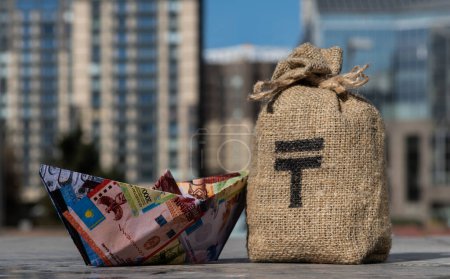 Money bag with Kazakhstani tenge symbol and paper boat made from Kazakhstani banknotes