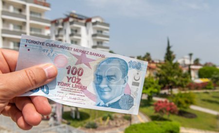 Banknote in denomination of 100 Turkish liras in a man's hand on the background of a Turkish landscape