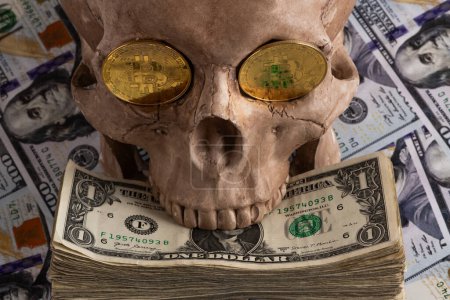 Téléchargez les photos : Une pièce d'or avec le symbole Bitcoin crypto-monnaie dans les orbites d'un crâne humain sur fond de billets de 100 dollars américains - en image libre de droit