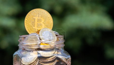 Téléchargez les photos : Pièce d'or avec Bitcoin symbole crypto-monnaie et pièces kazakhes de 100 et 200 coupures tenge dans un bocal en verre - en image libre de droit