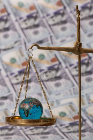 Photo for Glass miniature globe on the scales against the background of banknotes in denominations of 100 American dollars - Royalty Free Image