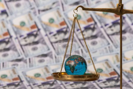 Photo for Glass miniature globe on the scales against the background of banknotes in denominations of 100 American dollars - Royalty Free Image