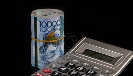 Taschenrechner und Banknoten im Wert von 10.000 kasachischen Tenge auf schwarzem Hintergrund
