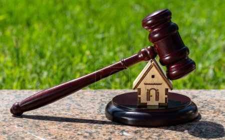 Téléchargez les photos : Symbolique maison en bois miniature et marteau du juge sur un fond naturel - en image libre de droit