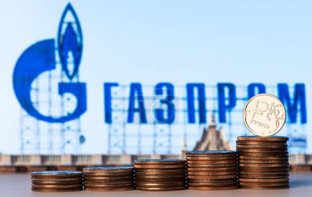 Photo for A coin with a denomination of 1 Russian steering wheel stands on a computer keyboard against the background of the Gazprom logo - Royalty Free Image