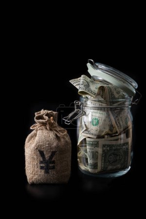 Money bag with Chinese Yuan symbol and glass jar filled with 1 US dollar bills