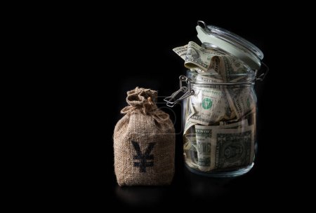 Money bag with Chinese Yuan symbol and glass jar filled with 1 US dollar bills