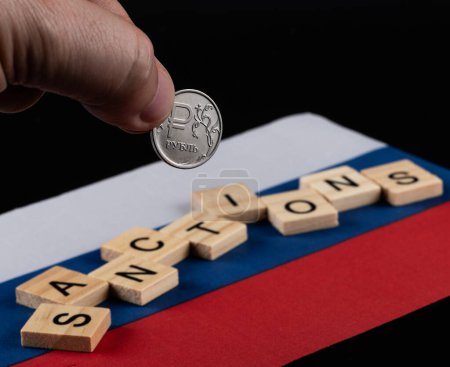 Münze mit dem Symbol des russischen Rubels, der Flagge Russlands und den Worten "Sanktionen"