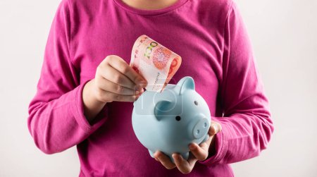Piggy bank and 100 Chinese yuan bill in children's hands