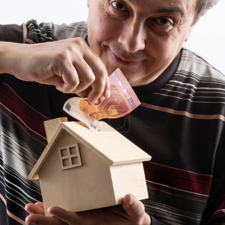 Middle-aged man, miniature wooden house and 10 euro note