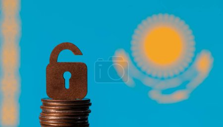 A symbolic wooden lock with a keyhole and a column of coins on the background of the flag of the Republic of Kazakhstan