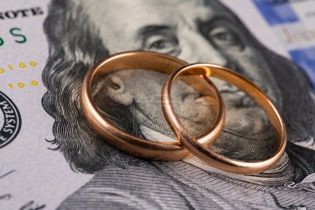 Gold wedding rings against the background of a fragment of a 100 US dollar bill