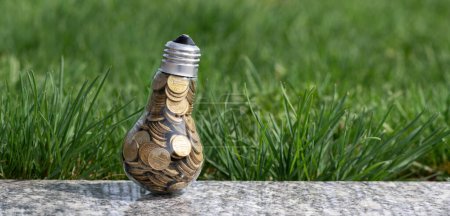 Una lámpara incandescente llena de 1 monedas de tenge kazajas sobre un fondo de hierba
