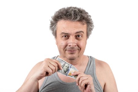 Ein zotteliger grauhaariger Mann mittleren Alters mit Stoppeln in einem ärmellosen T-Shirt hält einen 100-Dollar-Schein in seinen Händen.