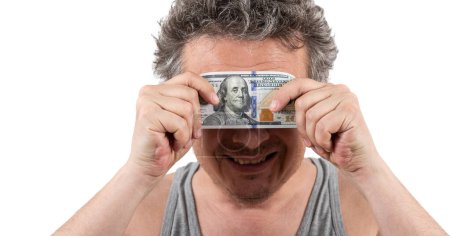 Photo for A shaggy gray-haired middle-aged man with stubble wearing a sleeveless T-shirt holds a 100 US dollar bill in his hands - Royalty Free Image