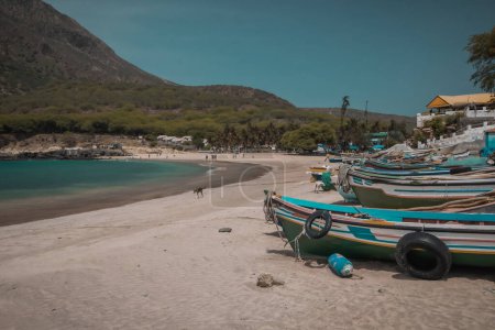 Téléchargez les photos : Bateaux en bois colorés sur une plage de l'île de Santiago sur les îles du Cap Vert, avec quelques arbres et maisons en arrière-plan. - en image libre de droit