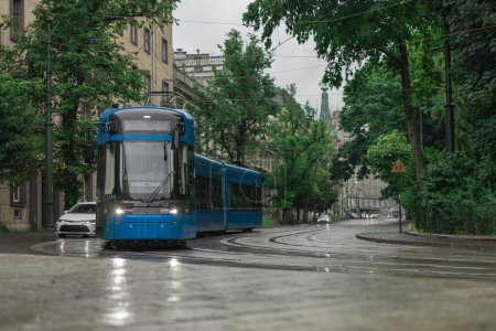 Photo for Blue polish tram in the middle of Krakow city on a rainy day. Beautiful picture of a tram, public service transport during a light drizzle rain - Royalty Free Image