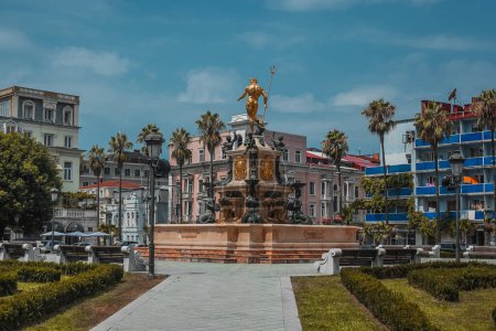 Foto de Parque central o plaza en el centro de Batumi, Georgia. Fuente de agua rodeada de diferentes edificios de colores y palmeras. Día soleado - Imagen libre de derechos