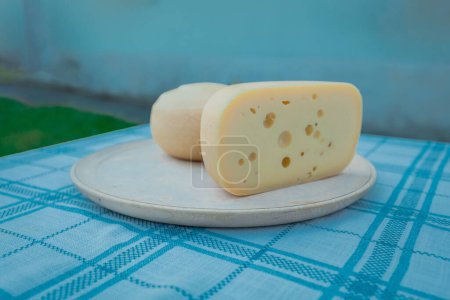 A block of cheese on a wooden plate and cute table. Slice of cheese with large holes and tasty core is visible. Lovely serving suggestion for a cheese.