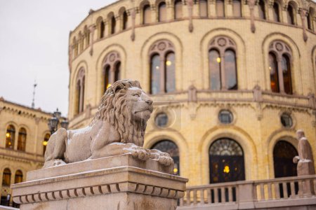 Téléchargez les photos : Statue d'un lion devant la maison du parlement nordique par une froide journée d'hiver. Lion reposant paisiblement sur un pilier devant un bâtiment majestueux. - en image libre de droit