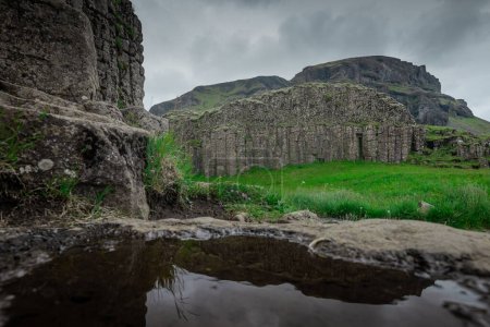 Basalt pillars rising from the ground in iceland, close to foss a sidu waterfall in southern part. Reflection of pillars in the small water pond.