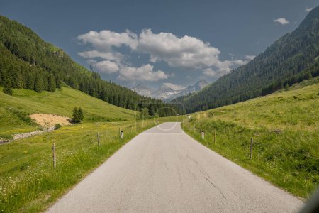 Die Straße in Richtung Solkpass in Österreich, einer der Gebirgspässe, wenn man Tunneln oder Obertauern ausweichen will. Grüne Hügel und ein paar Wolken im Hintergrund.