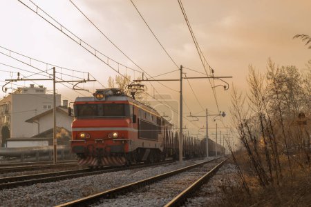 Foto de Tren de carga con locomotora roja y algunos vagones está conduciendo hacia la cámara en una mística puesta de la mañana temprano en el sol a punto de salir. - Imagen libre de derechos