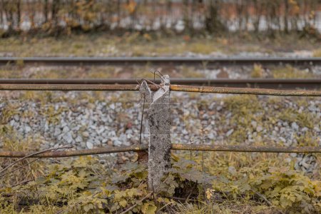 Clôture à côté d'une ancienne voie ferrée faite de tuyaux métalliques et de piliers en béton. Mauvais état de la clôture