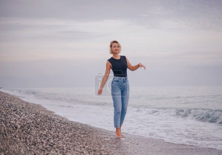 Foto de A slender woman in a beach walks along the seashore at sunset. - Imagen libre de derechos