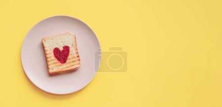 Téléchargez les photos : Heart shaped in tosted slice of rye bread on ceramic plate. Saint Valentine. breakfast concept. Yellow backgraund - en image libre de droit