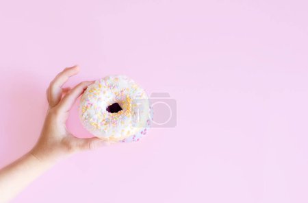 Foto de Cerca de la hembra sostiene en la mano colorido donut blanco sobre fondo rosa. Nutrición adecuada o dulces, postre comida rápida, dieta concepto de la mañana. Espacio de copia para publicidad. Área publicitaria - Imagen libre de derechos