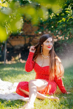 Téléchargez les photos : Smiling young woman wearing red dress and looking at camera. Beautiful tanned girl enjoying summer vacation . Portrait of stylish carefree woman - en image libre de droit