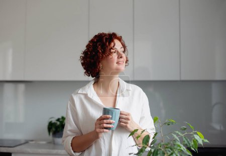 Photo for Portrait of joyful young woman enjoying a cup of coffee at home. Smiling pretty girl drinking hot tea - Royalty Free Image