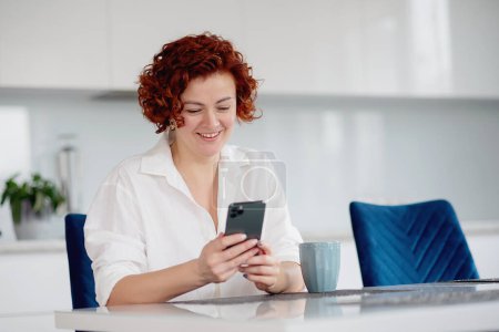 Téléchargez les photos : Girl checking social media holding smartphone at home. Smiling young woman using mobile phone app playing game, shopping online, ordering delivery - en image libre de droit