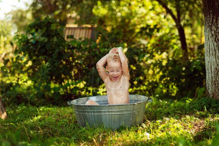 Téléchargez les photos : Little baby bathes in a basin, laughs and splashing his hands in water and making splashes. Summer days concept, holidays, rest, pool - en image libre de droit