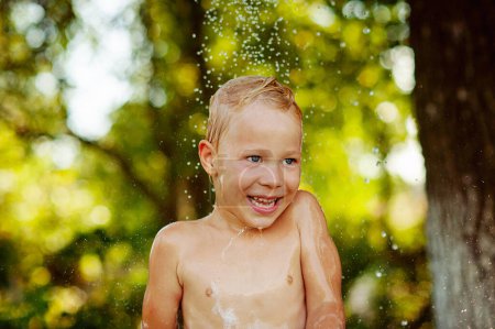Foto de Summer vacation in countryside, local staycation. Cute boy having fun, bathing and splashing in old iron bowl on the backyard , happy summertime, outdoor lifestyle - Imagen libre de derechos