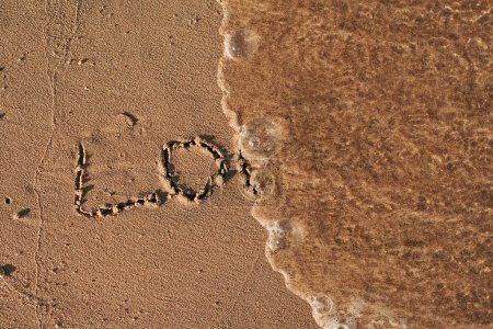 Téléchargez les photos : Des mots écrits dans du sable de plage. Le mot AMOUR écrit dans le sable sur la plage avec l'océan comme arrière-plan - en image libre de droit