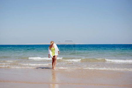 Téléchargez les photos : Femme sur la plage. Jeune femme heureuse marche le long du bord de la mer. La fille regarde la mer - en image libre de droit