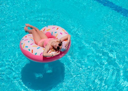 Photo for Young girl in a bathing suit relaxing on inflatable rubber ring in swimming pool. Enjoying summer. Vacation mood - Royalty Free Image