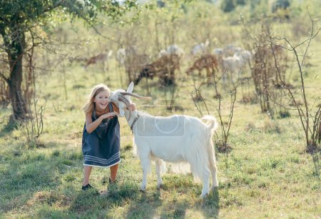Foto de Adorable chica jugando con cabras en la granja. Niña familiarizándose con los animales. Agricultura y jardinería. Actividades de verano al aire libre para niños - Imagen libre de derechos