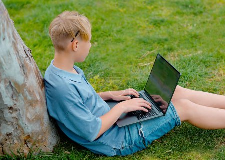 Foto de Adolescente está sentado en un parque con una computadora portátil y preparándose para las lecciones o exámenes. Concepto de formación y educación - Imagen libre de derechos
