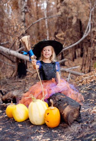 Téléchargez les photos : Drôle d'enfant fille en costume de sorcière pour Halloween avec des citrouilles - en image libre de droit
